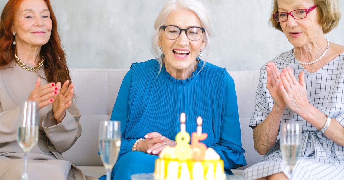 Can cake batter sit before using? - Positive elderly women in stylish clothes sitting on sofa near table with birthday cake and glasses of champagne celebrating birthday at home