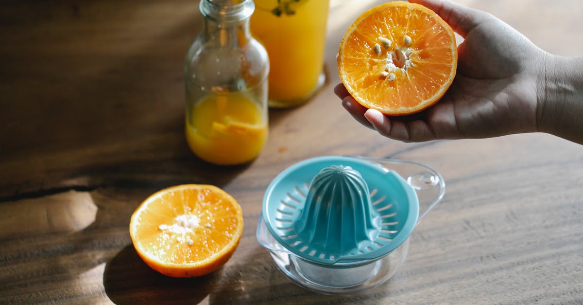 Can citrus be squeezed too much? - Crop anonymous person holding ripe citrus over wooden table with orange squeezer and glass bottle with fresh juice