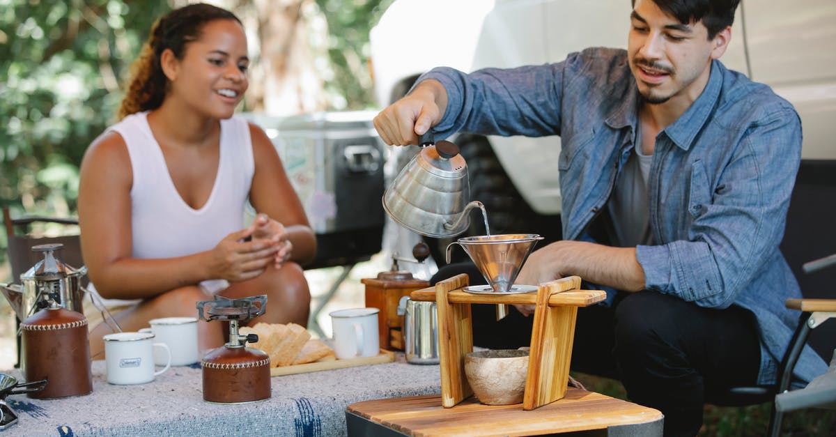 Can cold-brew coffee be heated? Why? - Content young man pouring hot water from gooseneck kettle into filter while preparing pour over coffee with smiling girlfriend during picnic