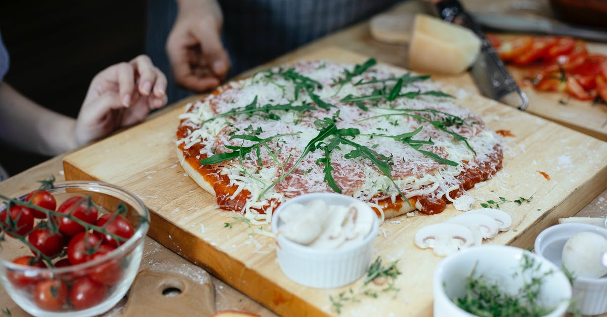 Can fresh basil cause tomato sauce spoilage? - Unrecognizable women and unbaked pizza with cheese and herbs on chopping board on table in kitchen