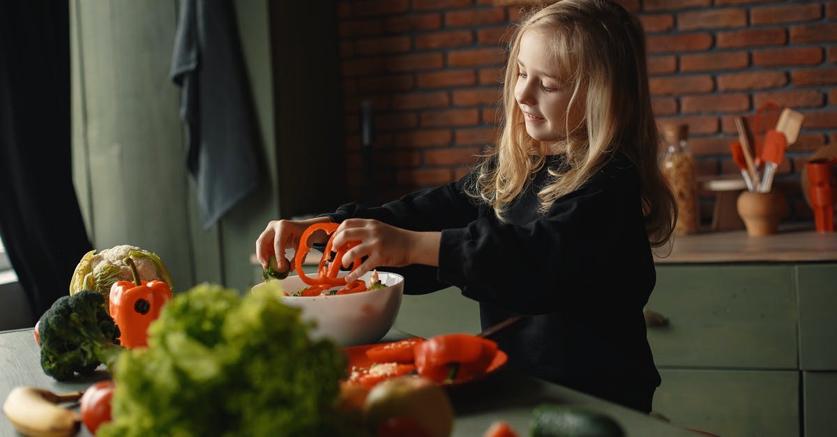 Can I add body to vegan stock with carrageenan? - Adorable smiling child adding sliced pepper in salad bowl standing near table with assorted vegetables and fruits during vegetarian meal preparation