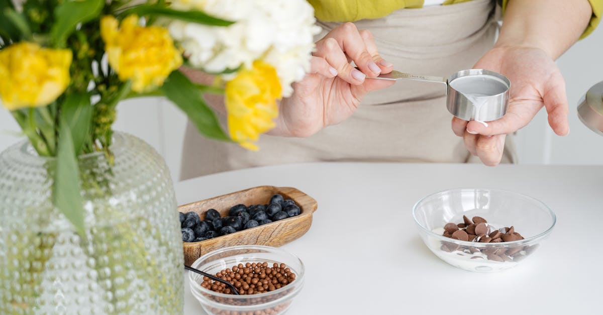 Can I add more cream to my thick and ready ganache? - Crop faceless female confectioner wearing apron and casual clothes adding hot ganache made of heavy cream from saucepan into chocolate drops in glass bowl