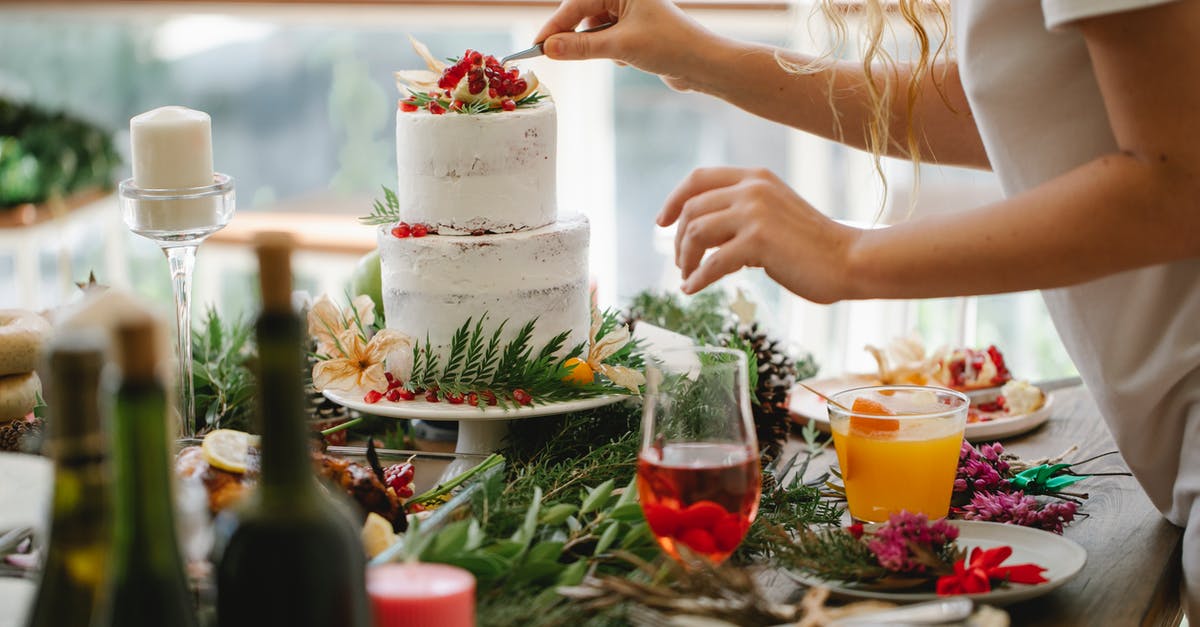 Can I bake a christmas cake in a cardboard box? - Crop anonymous female chef in casual clothes standing at table with various dishes and drinks and putting berries on top of delicious cake