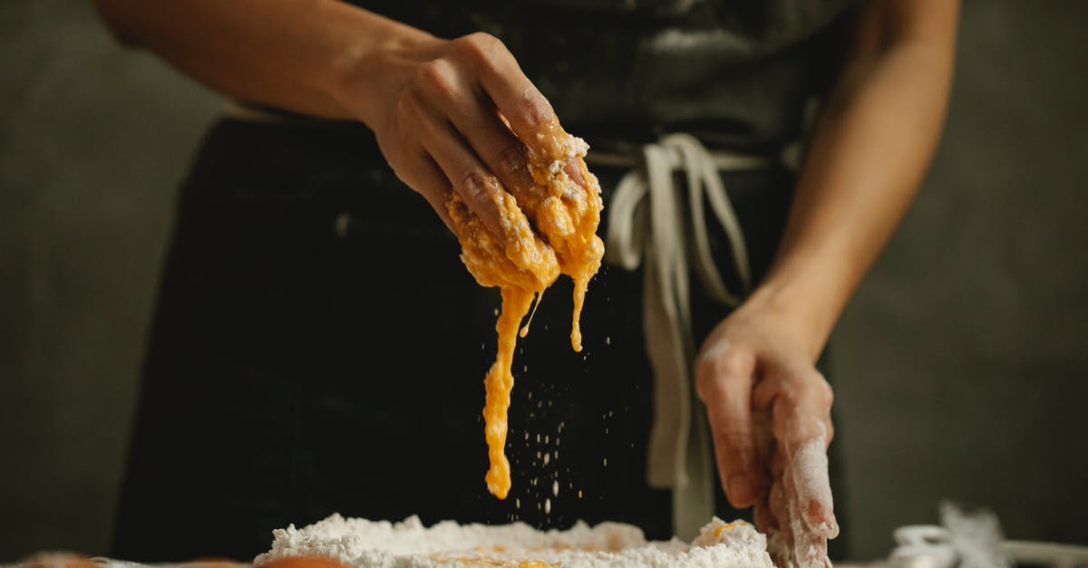 Can I bake a finished Ginger Bread House - Unrecognizable woman in apron kneading dough with eggs and flour on table in kitchen