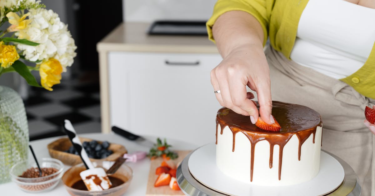 Can i freeze chocolate cream frosting / ganache? - Crop anonymous female confectioner putting slices on strawberry on cake with chocolate frosting