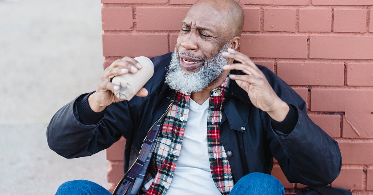 Can I get drunk by evaporating steam of alcohol? - African American bearded male in casual outfit raising arms with beer can while resting on street near brick wall