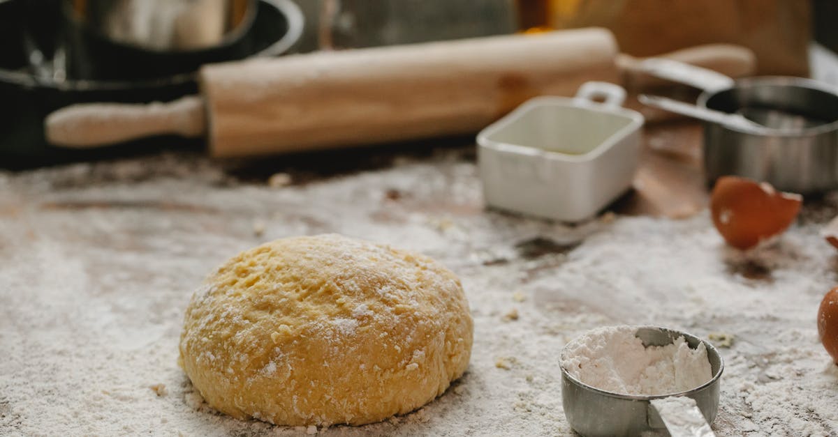 Can I make bread/pizza dough with only cricket flour and no wheat flour - Ball of raw dough placed on table sprinkled with flour near rolling pin dishware and measuring cup in kitchen on blurred background