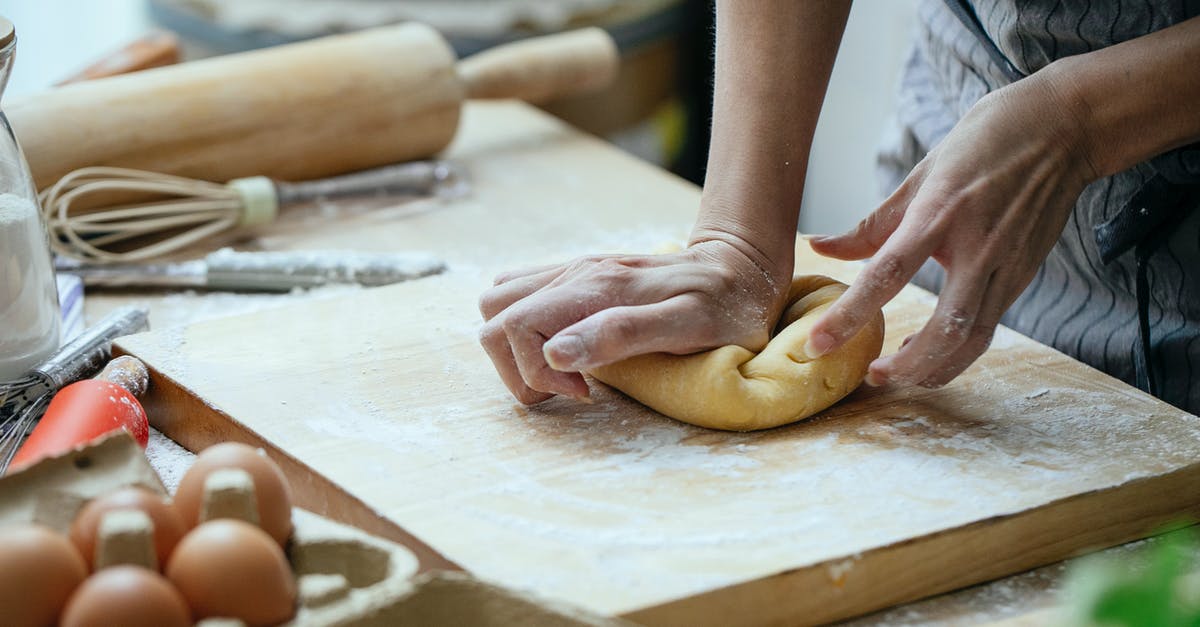 Can I make ciabatta with corn flour? - Unrecognizable female cook pressing piece of dough on wooden board while cooking at table with whisk and rolling pin against blurred background