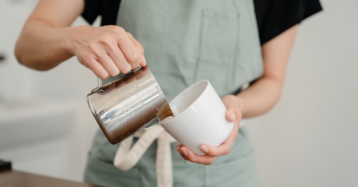 Can I make drinking milk with evaporated milk? - Crop unrecognizable barista in apron pouring milk from steel pitcher to white ceramic cup while preparing aromatic coffee in modern cafe