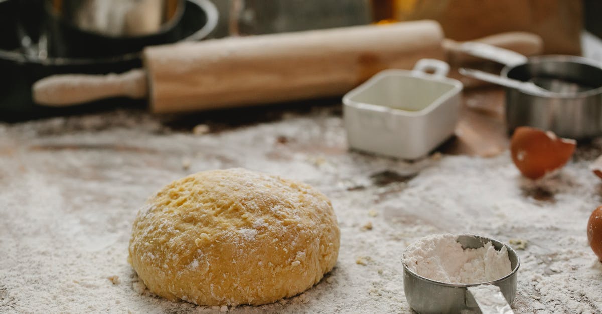 Can I make pasta with atta flour? - Ball of raw dough placed on table sprinkled with flour near rolling pin dishware and measuring cup in kitchen on blurred background