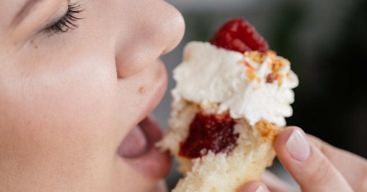 Can I refreeze defrosted crumb topping? - Crop unrecognizable female with closed eyes biting tasty sweet cupcake with with strawberry jam filing and decorated with whipped cream and berries