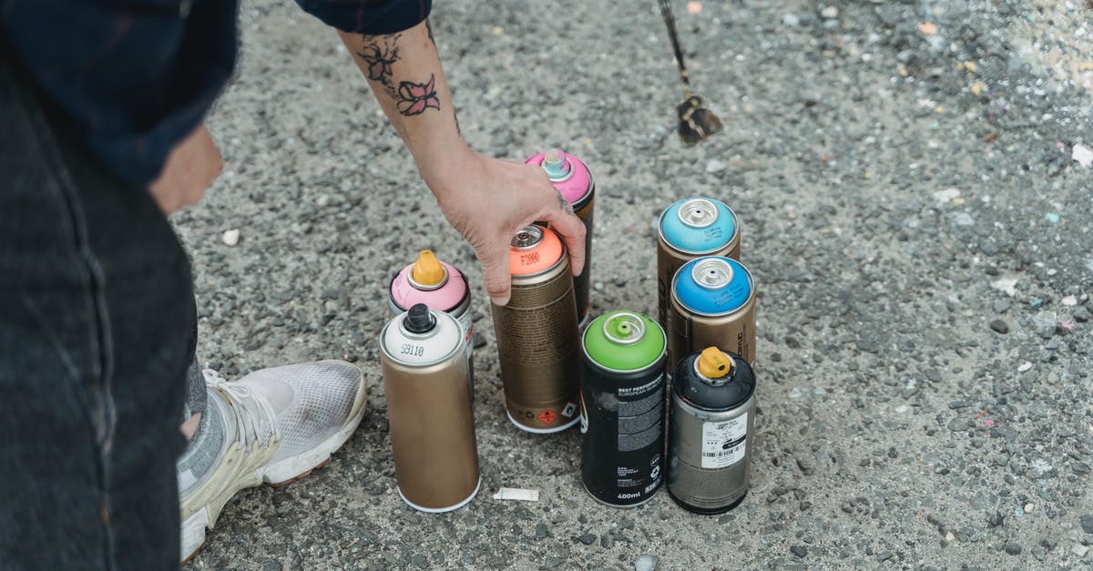 Can I weigh without a set of scales? - Crop faceless tattooed artist taking paint bottle from heap of multicolored spray cans placed on ground on street of city