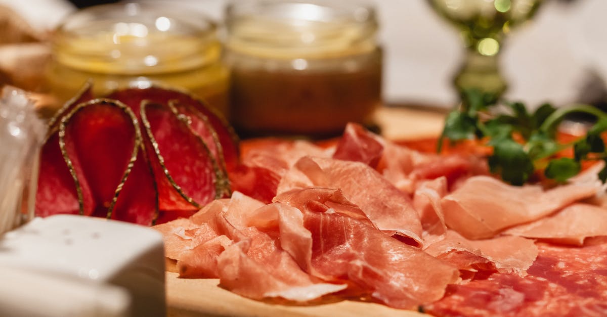 Can sourdough starter be used for tenderizing meat? - Delicious assorted cured sausage pieces on wooden tray between sauces and salt shaker on blurred background