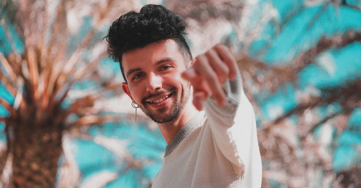 Can you eat acorns picked from the street? - Low angle of modern trendy man with earring pointing with finger at camera standing under palm trees in sunshine