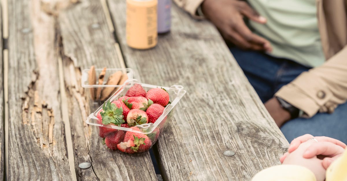 Can you identify this Serbian street food? - Crop anonymous couple sitting at shabby wooden table with strawberries and cookies near cans of soda while spending time in park