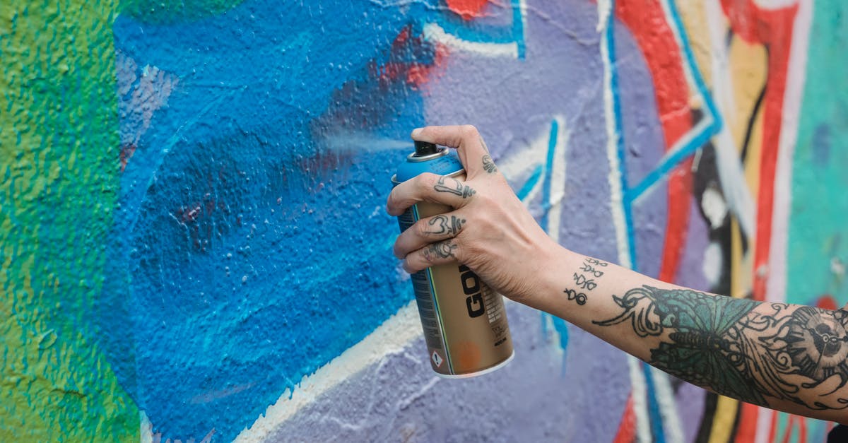 Can you identify this Serbian street food? - Crop unrecognizable tattooed painter spraying blue paint from can on multicolored wall with creative graffiti while standing on street in city