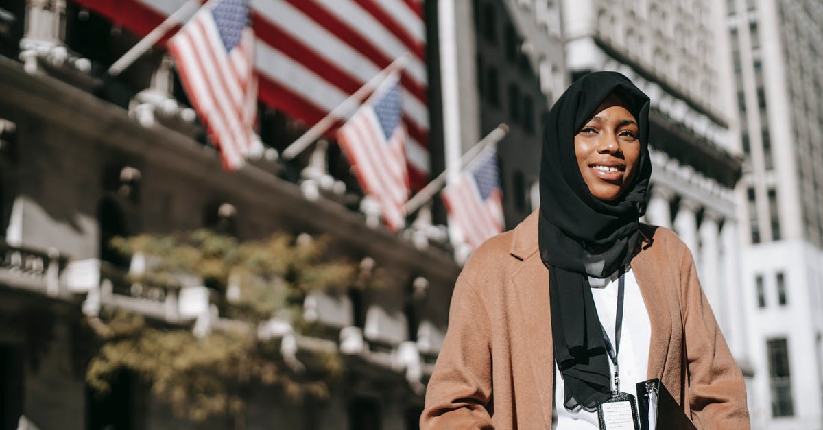 Can you identify this Serbian street food? - From below of cheerful African American female ambassador with folder wearing hijab and id card looking away while standing near building with American flags on blurred background