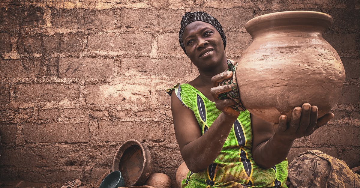 Can you put a clay pot into a preheated oven? - Smiling middle aged ethnic female in traditional dress and turban demonstrating handmade clay pot while sitting on street against shabby wall