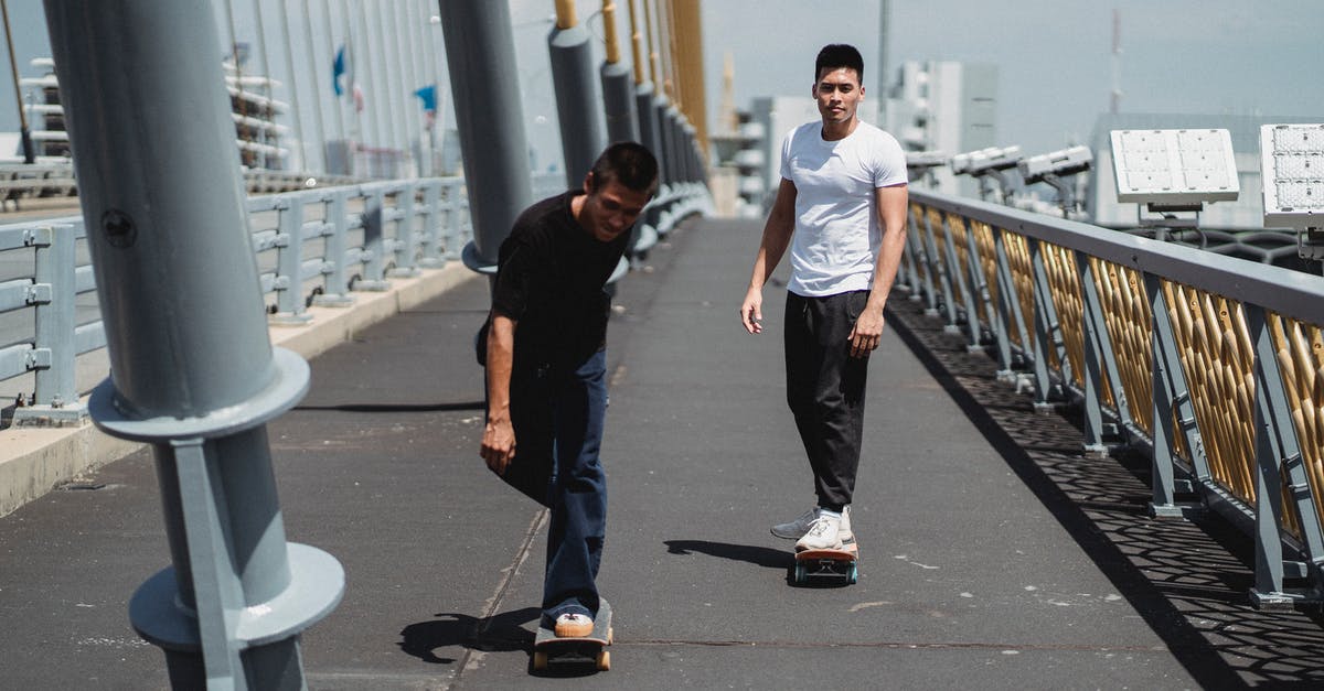 Cast Iron - Enamelled - Season or not? - Full body of young ethnic men skateboarding on asphalt bridge with metal constructions under cloudy sky