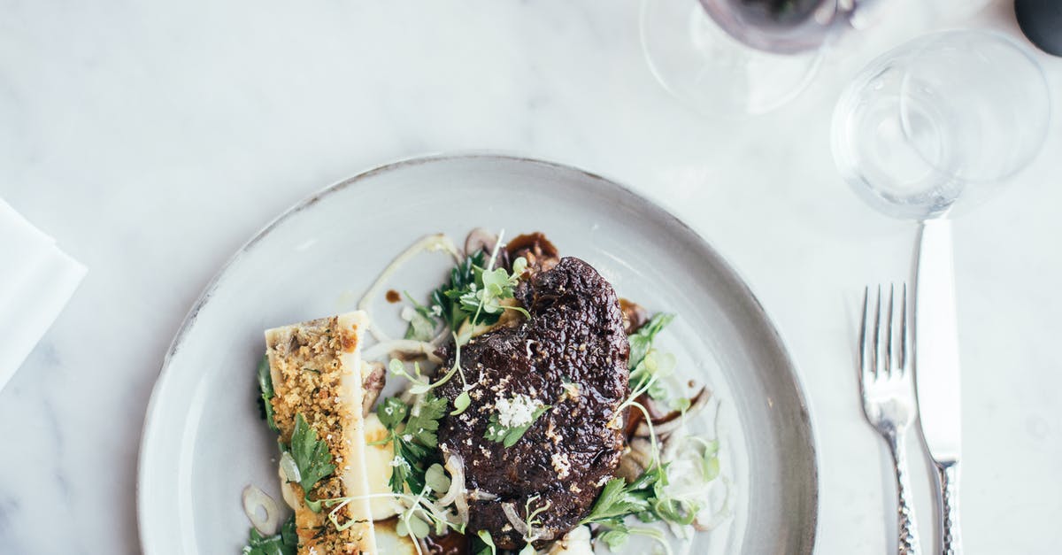 Celeriac (aka: Celery Root) Skin - Edible or Not? - Top view of delicious stuffed celery and grilled steal decorated with green herbs served on table with cutlery and glassware