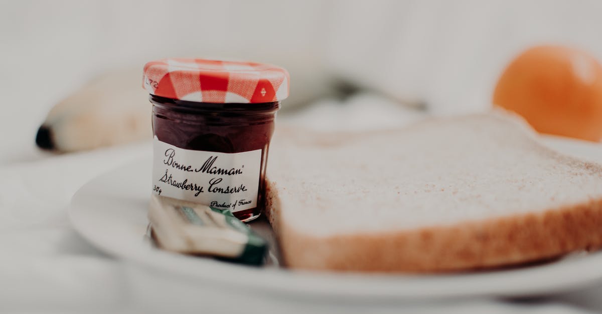 Cellophane lids on jam - Tasty marmalade in glass jar with written title near bread loaf for breakfast on plate
