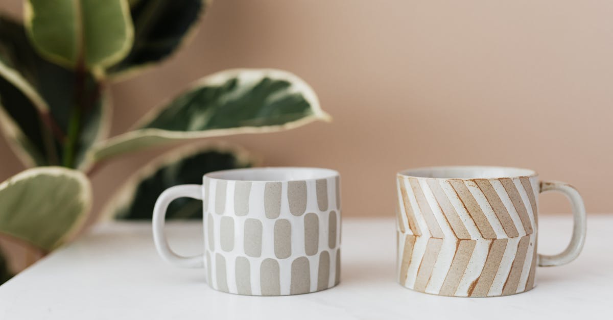 Ceramic Coffee mug measurement - Handmade ceramic mugs with creative designs placed on white marble table with blurred green house plant near pink wall in background