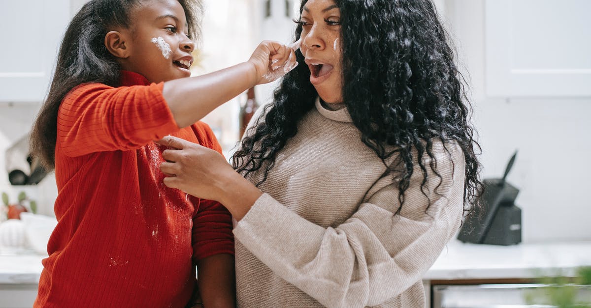 Changing Protein Content of Flour - Positive dirty ethnic child applying flour on face of young crop parent while having fun in kitchen and looking at each other