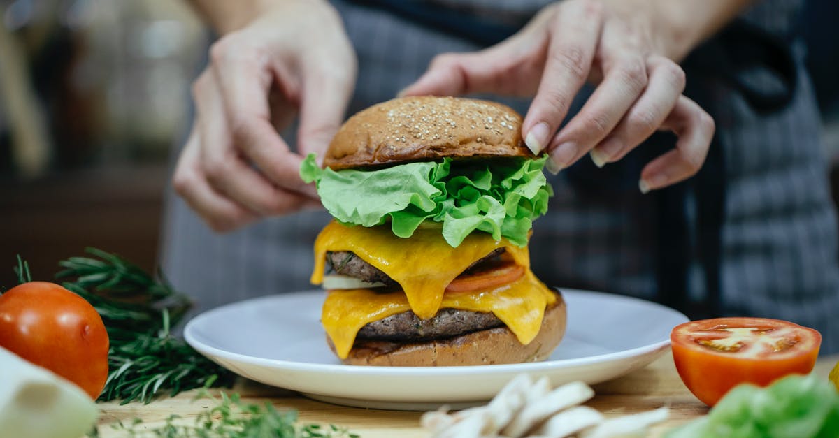 Cheese suggestions to replace melted Velveeta - Faceless female chef preparing delicious double cheeseburger with bread buns and meat patties between fresh vegetables and herbs at home