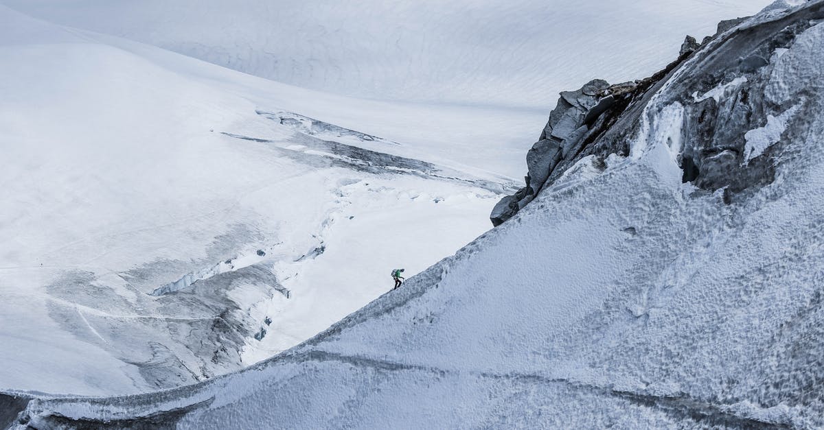 Chiffon gets stiff overnight - From above distant alpinist on snowy rough mountain slope against frozen spacious mountainous valley in daylight