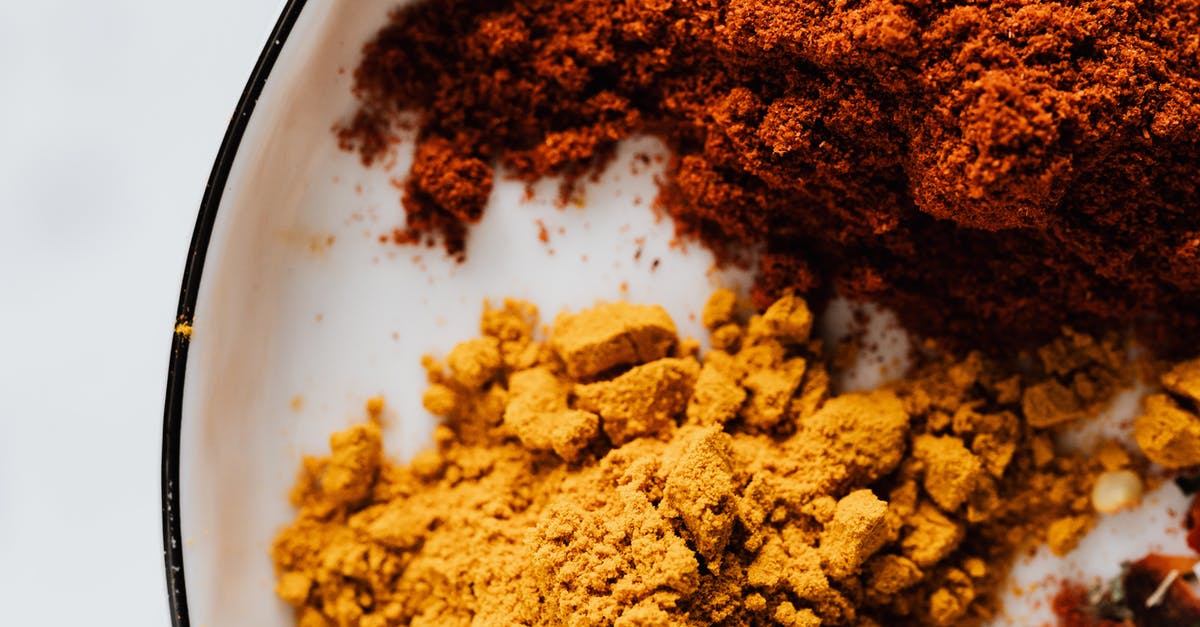 Chili ended up tasting like indian food - Top view of small heaps of ground chili and curcuma powders in metal bowl on white surface