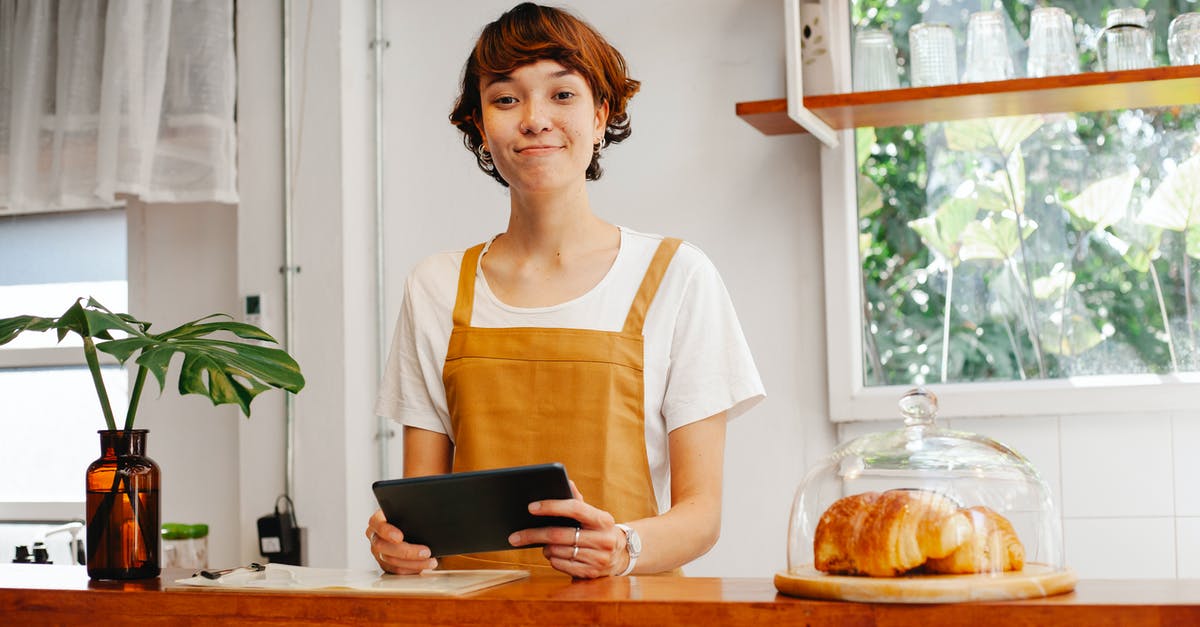 Chilled puff pastry vs frozen - Sincere young female cafeteria worker with tablet looking at camera near container with tasty pastries