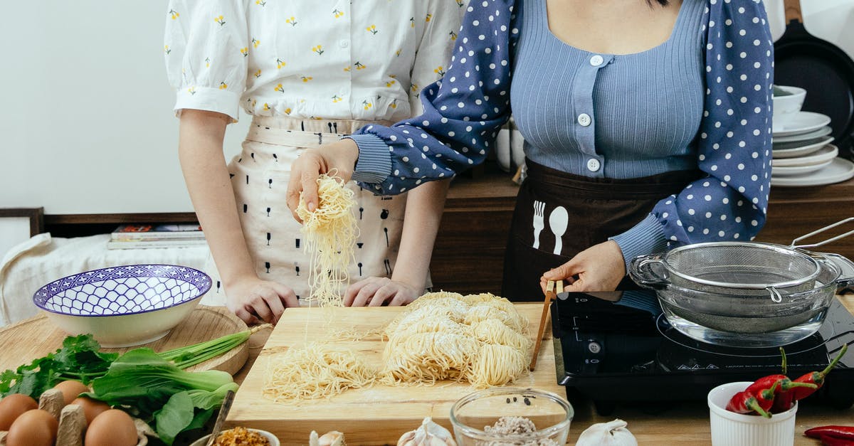 Chinese noodle dough breaking when pulled - Crop anonymous ladies in aprons standing near wooden table with various ingredients and utensil while preparing to cook homemade pasta together