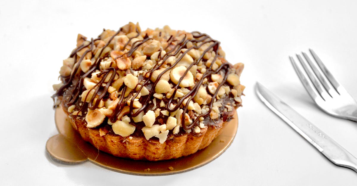 Chocolate hazelnut: efficacy of mixing crushed&roasted hazelnuts to sauce - Appetizing sweet pie tart with shortcrust pastry and chopped nuts topped with chocolate sauce on white background near fork and knife