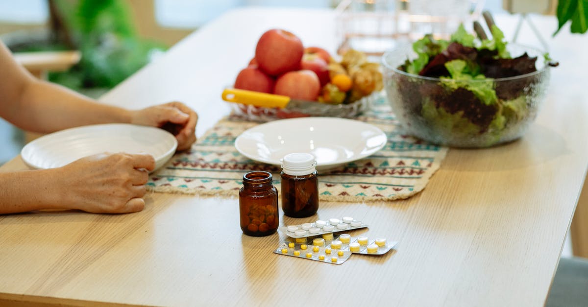 Choricitos a la sidra -- raw or cured? - From above of crop anonymous person sitting at table with pile of various medicines and bowls of fresh lettuce salad and ripe fruits in kitchen