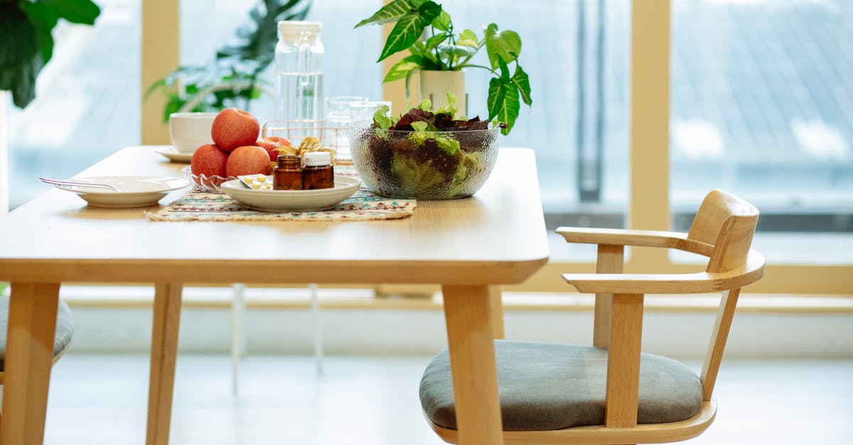 Choricitos a la sidra -- raw or cured? - Plates with medicines and ripe apples and bowl of fresh lettuce salad placed on wooden table near potted plant and bottle of water