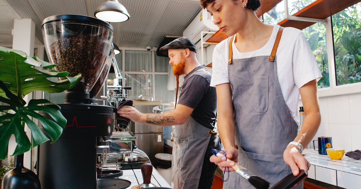 Cleaning burr coffee grinder - Crop baristas against coffee maker and grinder in cafe kitchen