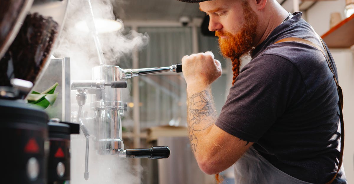 Cleaning burr coffee grinder - Crop employee cleaning espresso maker with vapor at work