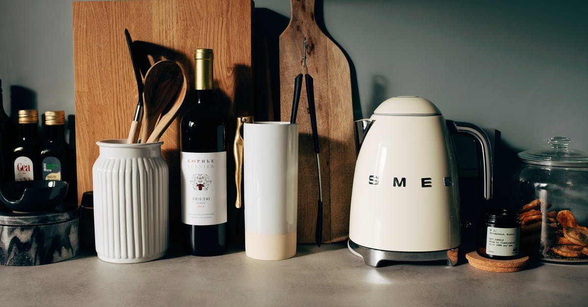 Cleaning dark stone kitchen countertops - White gloss electric kettle standing next to other kitchen utensils with bottle of wine and various bowls on countertop in modern home kitchen