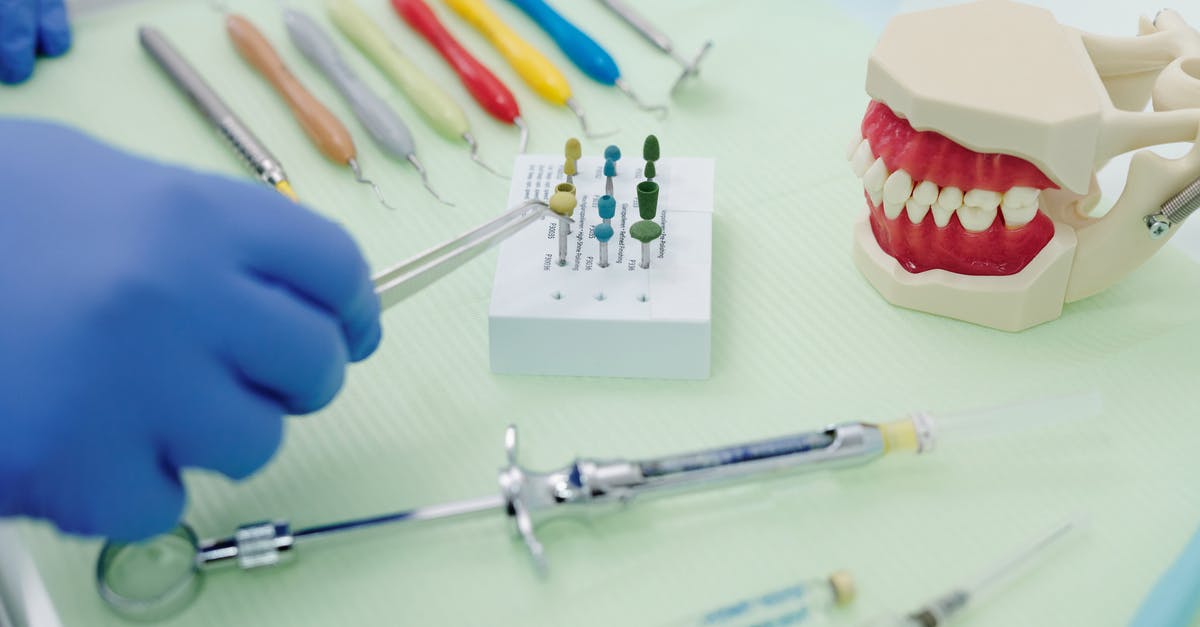 Cleaning my cast iron from exploded battery and plastic - From above of crop faceless orthodontist in latex gloves and tweezers working at medical table with cast jaw and set of syringes near periodontal scalers