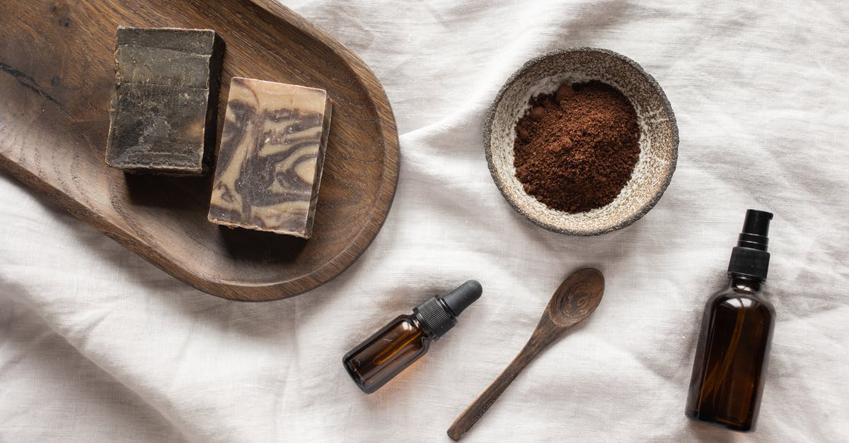 Cleaning out a smell - Top view of coffee scrub in bowl composed with bottles of aromatic oil on white sheet