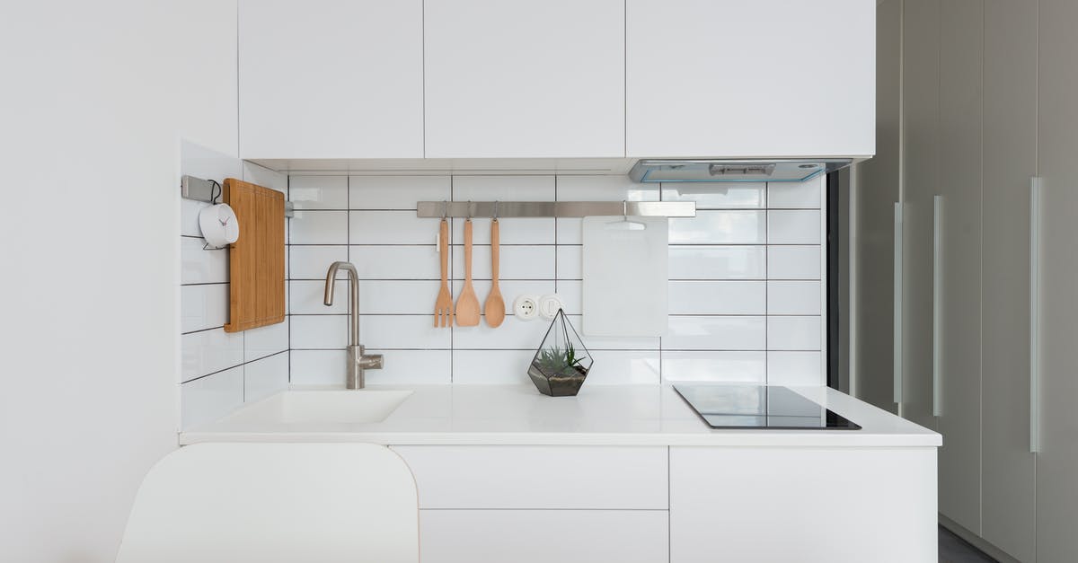 Cleaning white bubbles on induction stove - Wooden table placed near white cupboards in modern kitchen with minimalist interior in daylight