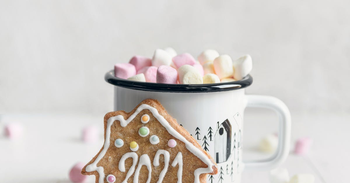 Coffee flavored melted chocolate for drizzling over cookies? - Festive gingerbread cookie with inscription 2021 placed against mug of delicious hot drink garnished with sweet marshmallows and served on white table