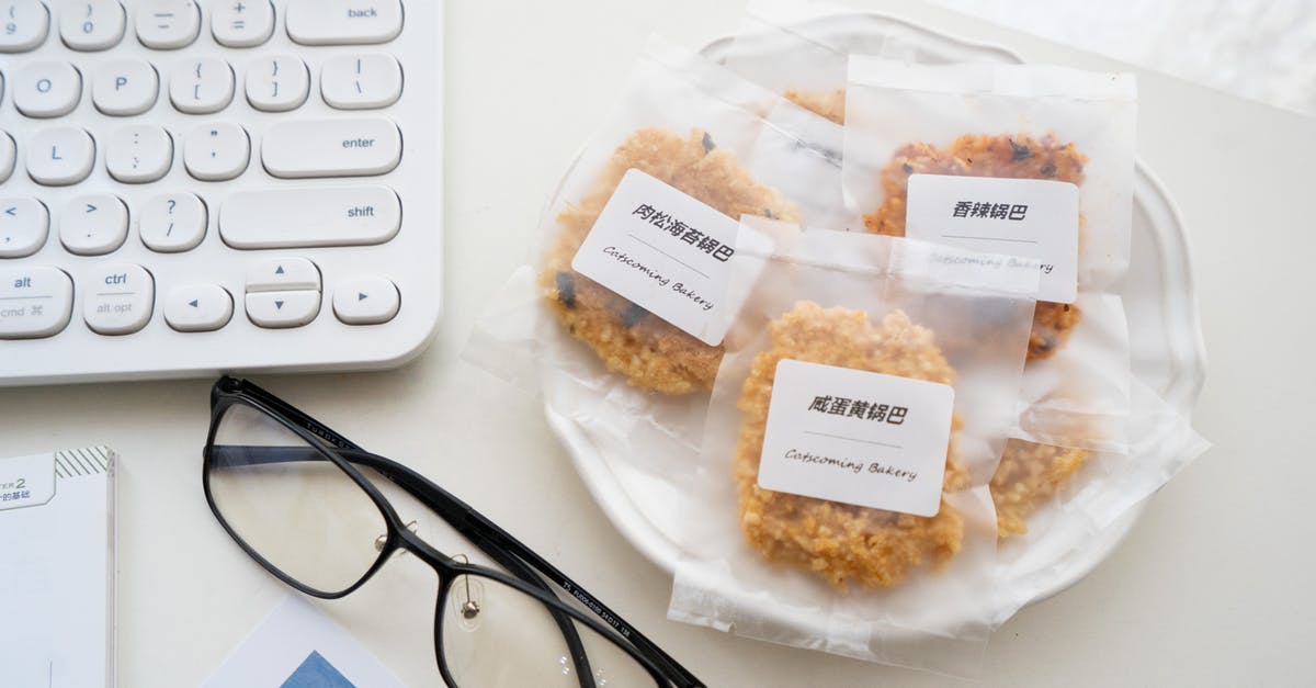 Commerial-grade packaging (long shelf-life) for my cookie-like pastry - Top view composition of cookies in individual packages with label served on ceramic plate near eyewear and keyboard of computer placed on white table