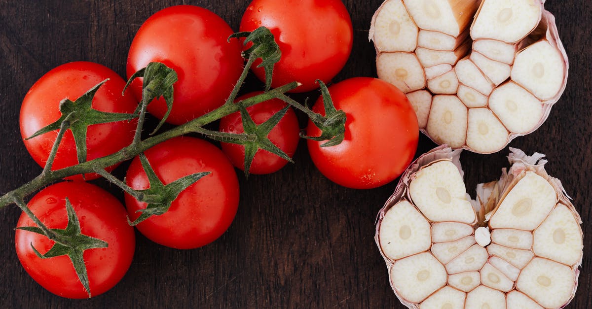 Comparing store-bought chopped garlic - From above of branch of ripe tomatoes and cut garlic on halves placed on wooden table