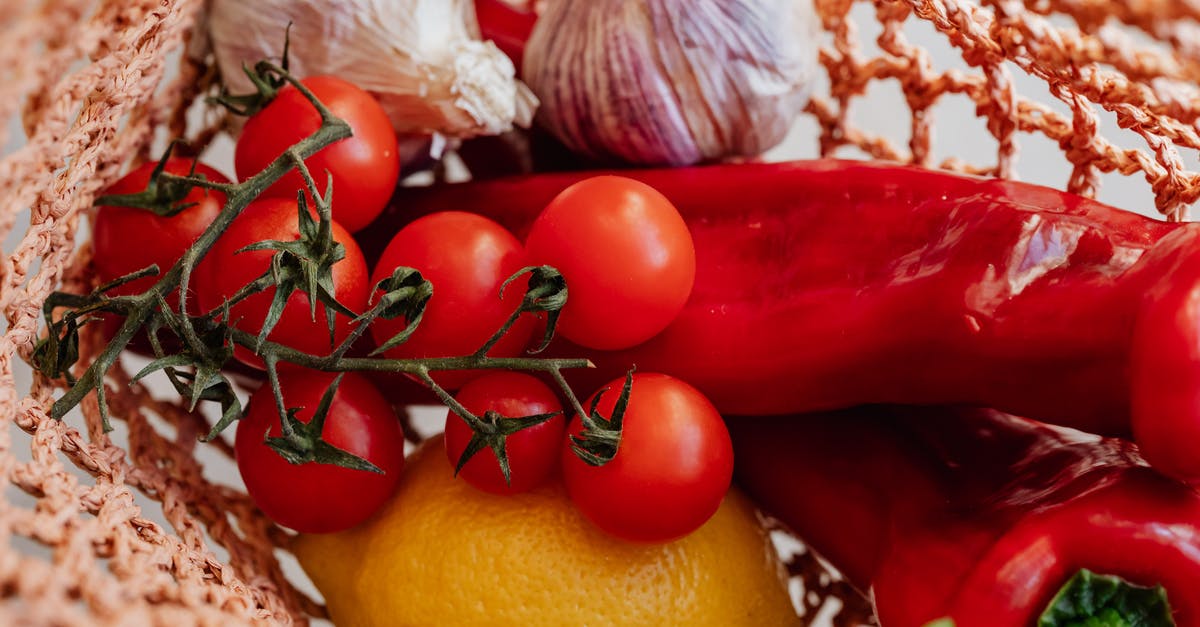 Composition/safety of cherry pits - Top view of ripe tomatoes on branch arranged amidst fresh yellow lemon and red chili peppers with garlic in pink food net