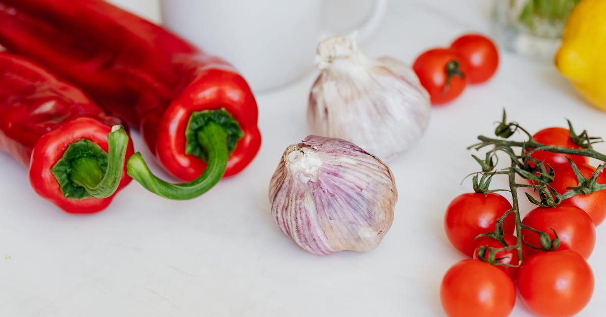 Composition/safety of cherry pits - Fresh garlic placed among ripe red cherry tomatoes and peppers on white table near white ceramic cup and yellow lemon