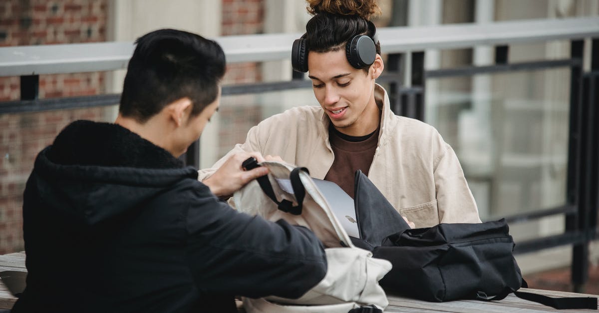 Concentrated Yerba Mate - Focused male students in casual outfits sitting at table and talking about new project while taking out laptops from backpacks