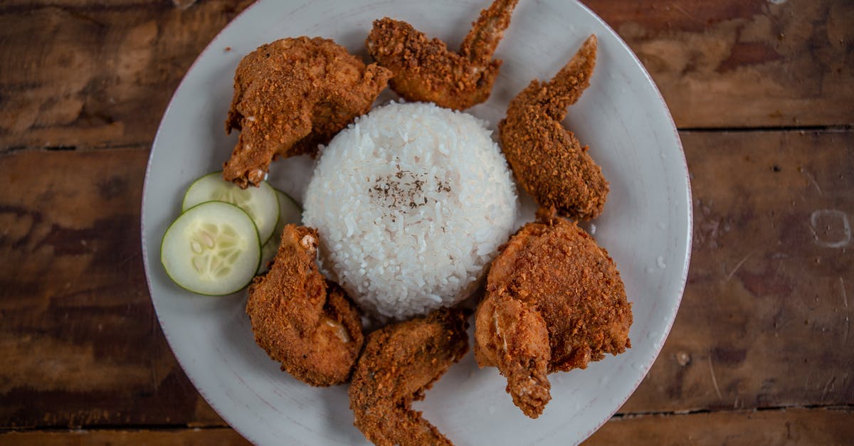Confirming Fried Chicken is completely cooked - Top view of appetizing golden chicken wings with cooked rice and cucumber slices on wooden table