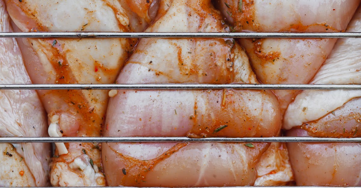 Confusion about chicken leg & thighs nutrition facts (calories) - From above of closeup of raw chicken legs with seasoning cooking on metal grill grate