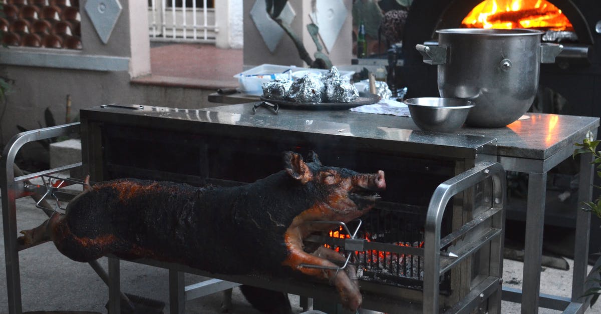 Cook kan-kan pork-chop in BBQ - Whole smoked pig on broach near metal table with various utensils in yard of countryside house